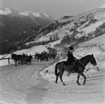 Mann mit Zylinder auf Pferd, hinten Schlittentross