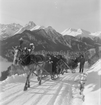 Festlicher Pferdeschlittentross auf verschneiter Bergstrasse