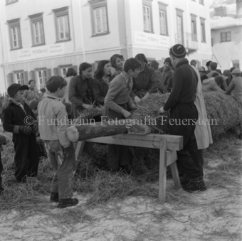 Kinder in Strohhaufen auf Dorfplatz, Stroh um Stamm wickelnd