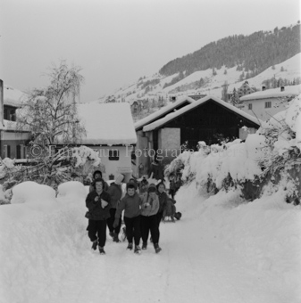 Kinder ziehen mit Schlitten die verschneite Dorfstrasse hoch