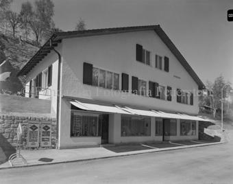 Haus Coiffeur Müller, Foto Feuerstein-Vitrine mit Bildern und Kamera neben anderen Schaufenstern, Sonnenstoren
