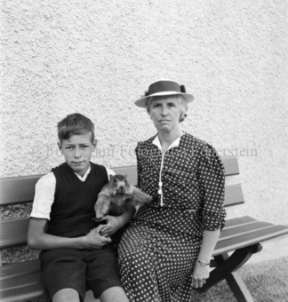 Frau und Junge mit Murmeltier in den Armen auf Sitzbank