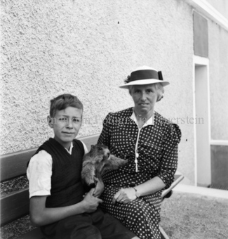 Frau und Junge mit Murmeltier in den Armen auf Sitzbank