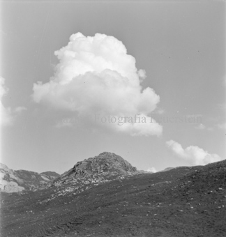 Berghang mit bröckeligem Gipfel, darüber Wolke