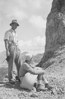 Frau sitzend auf geröllbedecktem Boden, Mann mit Fernglas, Felswand