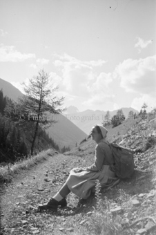 Frau mit Rucksack an Wanderweg sitzend