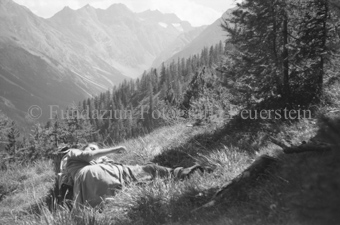 Frau auf Berghangwiese liegend, hinten Wald und Berge