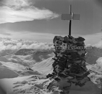 Steinmann mit Kreuz als Markierung auf Berg oben, verschneite Berglandschaft