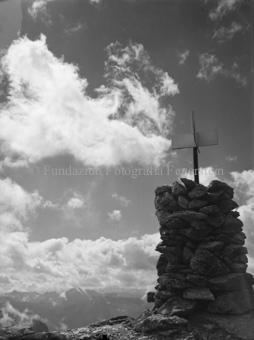 Steinmann mit Kreuz als Markierung auf Berg oben,  Wolken und viele Alpengipfel