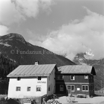 Gasthaus, Tische und Bänke, Holzhaufen und Zaun, Berge hinten
