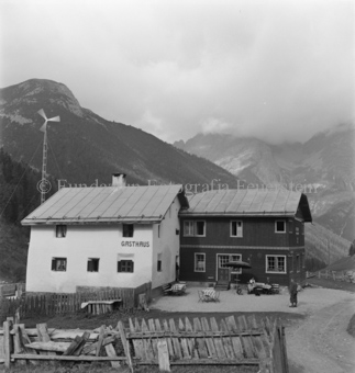 Gasthaus, Tische und Bänke, Holzzaun und Windrad, Berge hinten