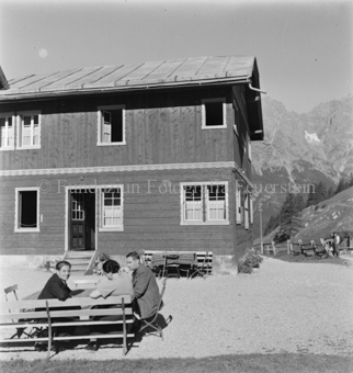 Drei Menschen an Tisch auf Platz vor Gasthaus