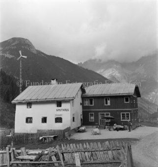 Gasthaus, Tische und Bänke, Holzzaun und Windrad, Berge hinten