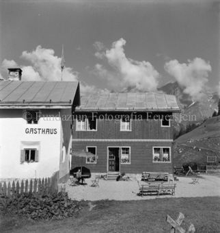 Gasthaus, davor Kiesplatz mit Stühlen und Bänken, Junge an Tisch