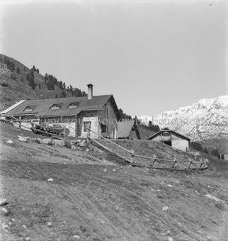 Häuser an Berghang, Holzzaun, hinten verschneite Berge