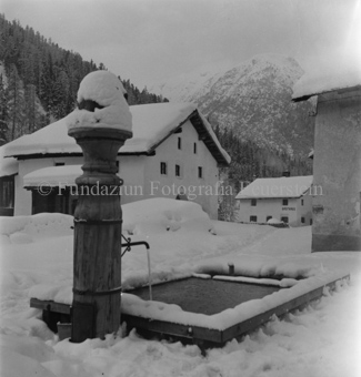 Schneebedecktes Dorf und Brunnen mit Skulptur