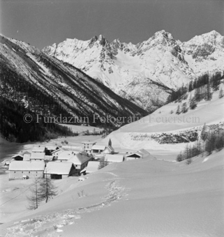 Verschneites Dorf in Tal, Wald und Berge im Hintergrund