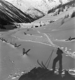Spuren in Schnee zu eingeschneitem Dorf, Schatten von Skitourengänger