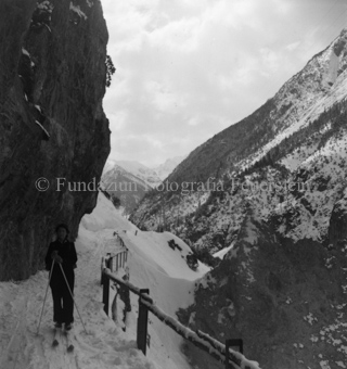 Skitourengängerin auf verschneitem Weg bei Klippe, Schutzzaun