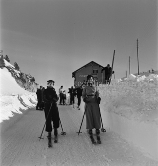 Skifahrergruppe auf schneebedeckter Strasse vor Gasthaus auf Ofenpass