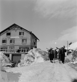 Gasthaus auf Ofenpass, Gruppe mit Skis auf den Schultern läuft über Strasse