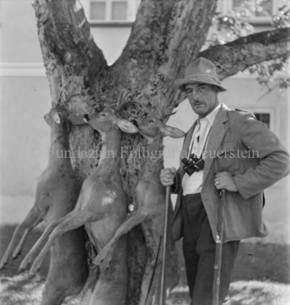 Jäger neben Baum mit drei aufgehängtnen toten Rehböcken, Fernglas um den Hals