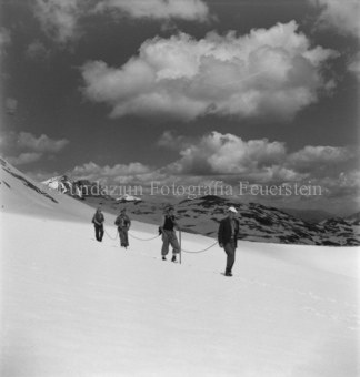 Vier Bergsteiger mit Seil im Schnee, Wolken und Schatten