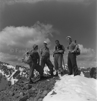 Vier Bergsteiger auf Berg stehend, hinten Wolken und Berge