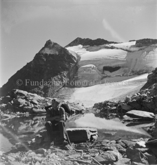 auf Felsbrocken sitzender Bergsteiger bei Gletscher
