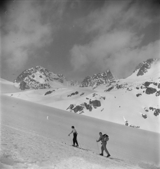 Skitourengänger und Skitourengängerin den Hang hinauf, hinten Gipfel