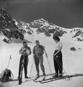 Mann und Frau auf Ski, dritter Ski in der Hand, Berggipfel