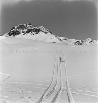 Skifahrer in Skispur an Hang fahrend, hinten Berggipfel
