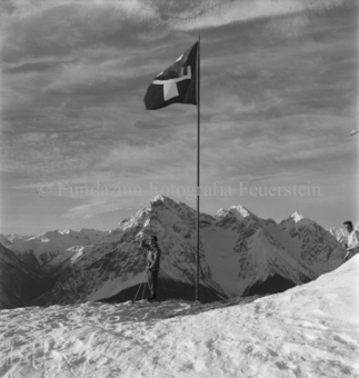 Skitourengänger neben Schweizerfahne, Bergpanorama