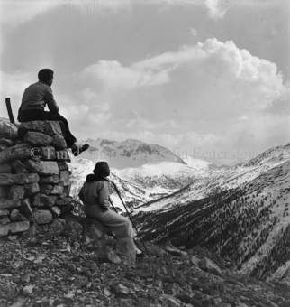 Mann auf, Frau an Steinmann sitzend, Blick auf Berglandschaft, Wolken