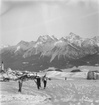 Drei Skifahrerinnen vor Dorf, Bergpanorama