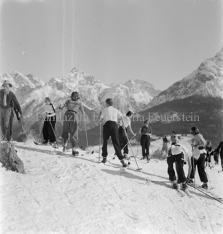 Mehrere Skifahrerinnen und Skifahrer, in unterschiedliche Richtungen fahrend, Bergpanorama
