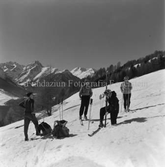 Skitourengänger und drei Skitourengängerinnen mit Sonnenbrille an Hang, im Hintergrund Wald und Berge