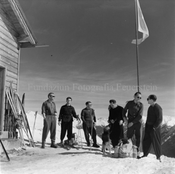 Gruppe Skitourengänger mit Hund neben Berghütte, Ski an Wand, Fahnenmast mit Schweizer Fahne
