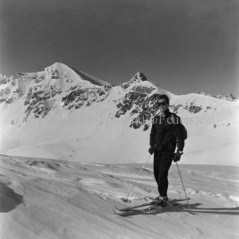 Skifahrer mit Sonnenbrille und Rucksack, hinten Berggipfel