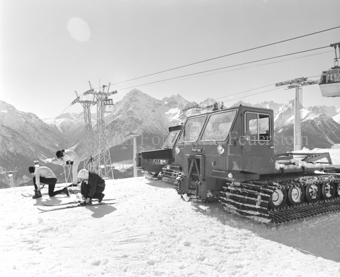Skifahrer neben Pistenfahrzeugen bei Gondelseilbahn