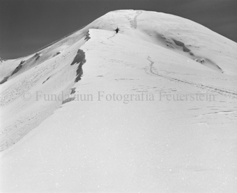 Wanderer mit Ski auf dem Rücken im Schnee, bergauf