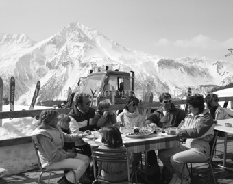 Personen auf Restaurantterrasse, Pistenfahrzeug im Hintergrund