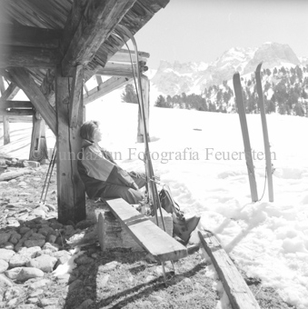 Frau auf Bank vor Hütte, Schneelandschaft, Ski im Schnee