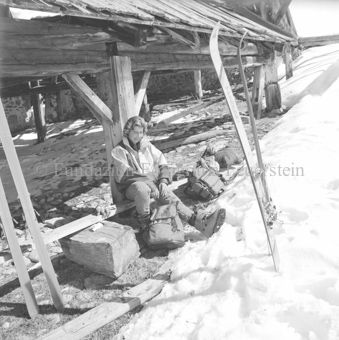 Frau auf Bank vor Hütte, Schneelandschaft, Ski im Schnee