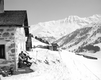 Skitourengänger auf Bank vor Berghütte, Schneelandschaft
