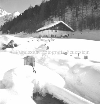 vereister Brunnen, verschneite Hütte und Landschaft mit Weg vom Brunnen zur Hütte