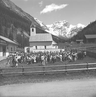 Versammlung vor Kirche in S-charl, Berglandschaft im Hintergrund