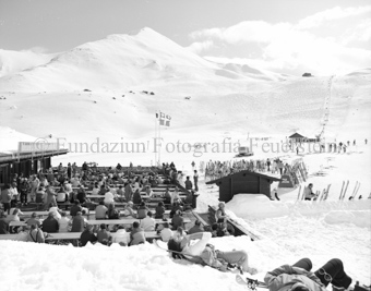 Personen auf Tischen und Bänken bei Bergrestaurant auf Alp Trida, Schlepplift im Hintergrund
