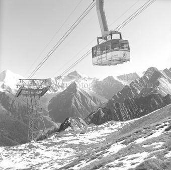 Luftseilbahngondel vor Berglandschaft, zum Teil schneebedeckt