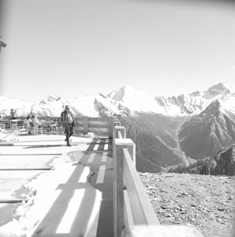 Personen auf Terrasse bei Berghütte mit Aussicht auf Berglandschaft